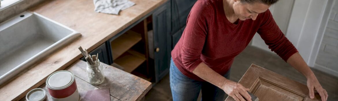 Woman sanding kitchen cabinet door indoors