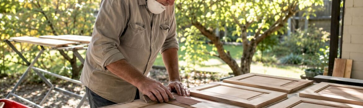 Man sanding multiple cabinet doors in workshop