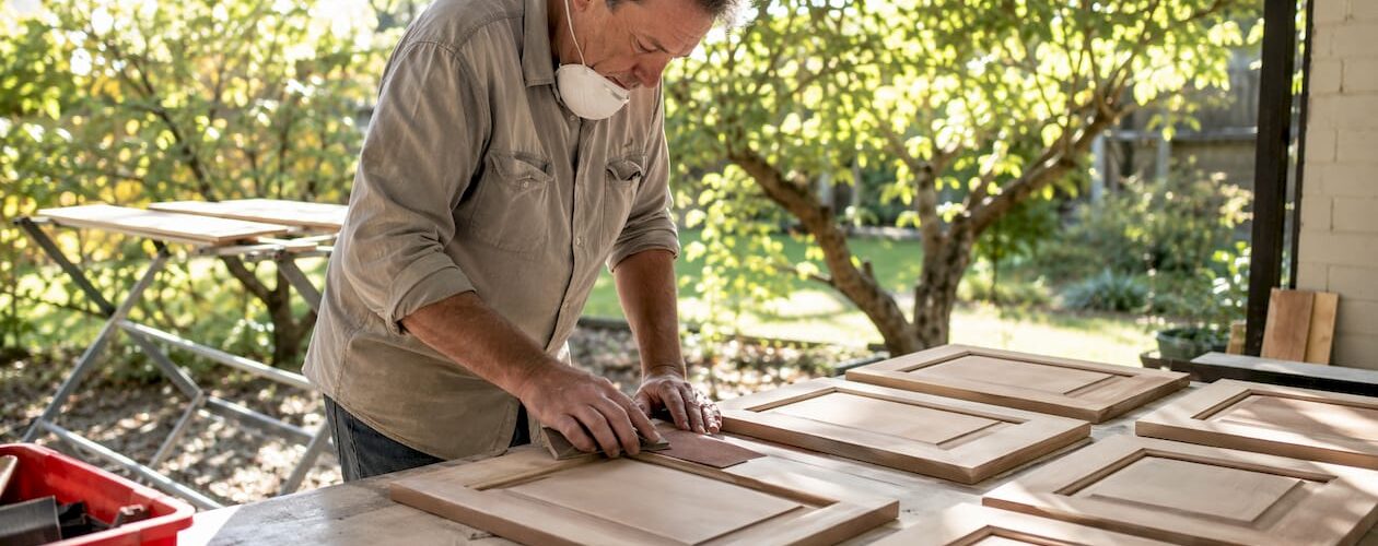 Man sanding multiple cabinet doors in workshop