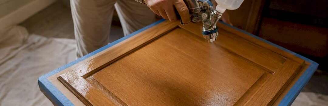 Hands spraying water-based finish on cabinet door