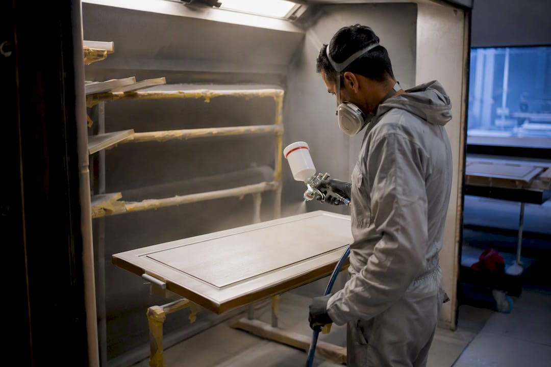 Technician spray-finishing detached cabinet door