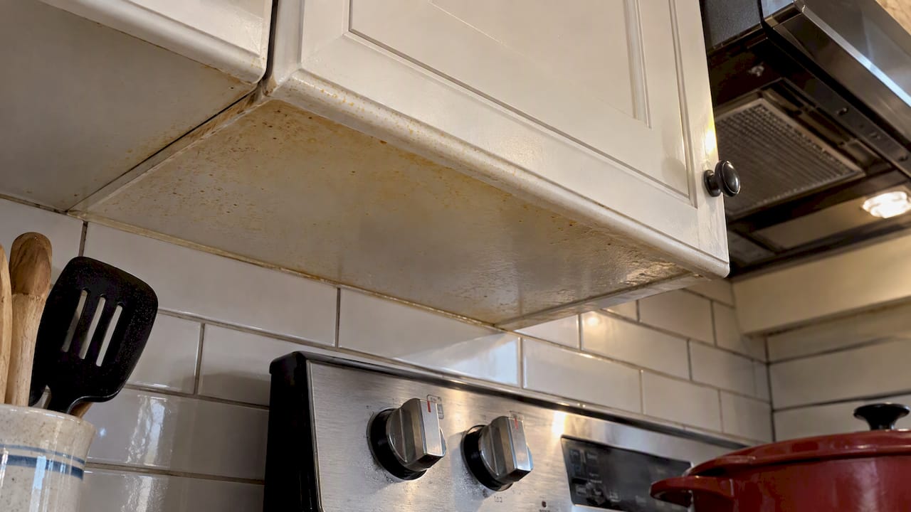 Grease film beneath white cabinets near stove